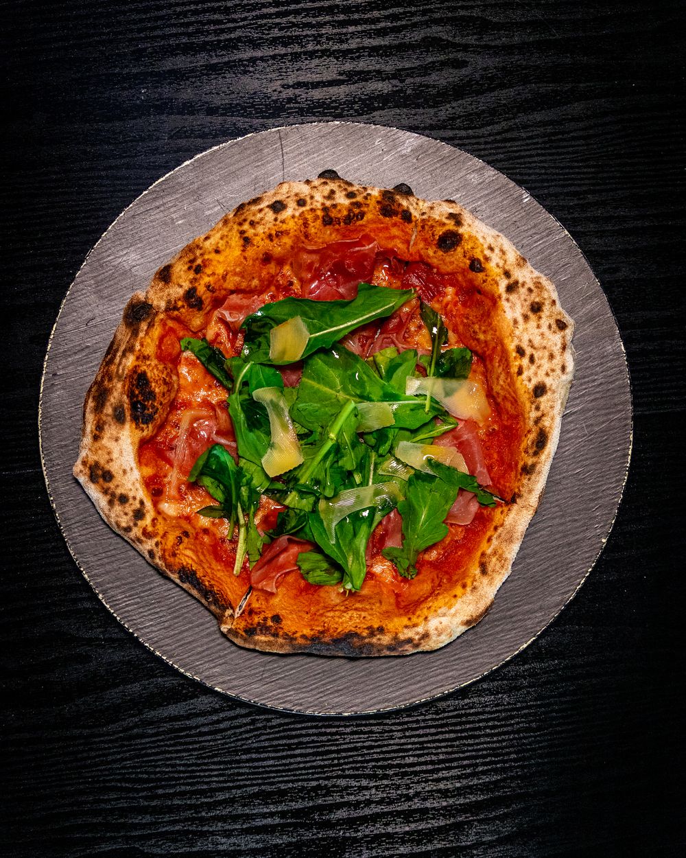 Pizza de prosciutto y rúcula de masa madre sobre piedra, vista desde arriba