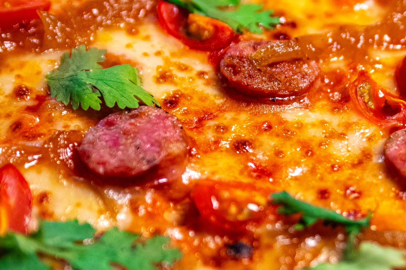 Detalle del chorizo dorado y el cilantro sobre la pizza de chorizo y tomate