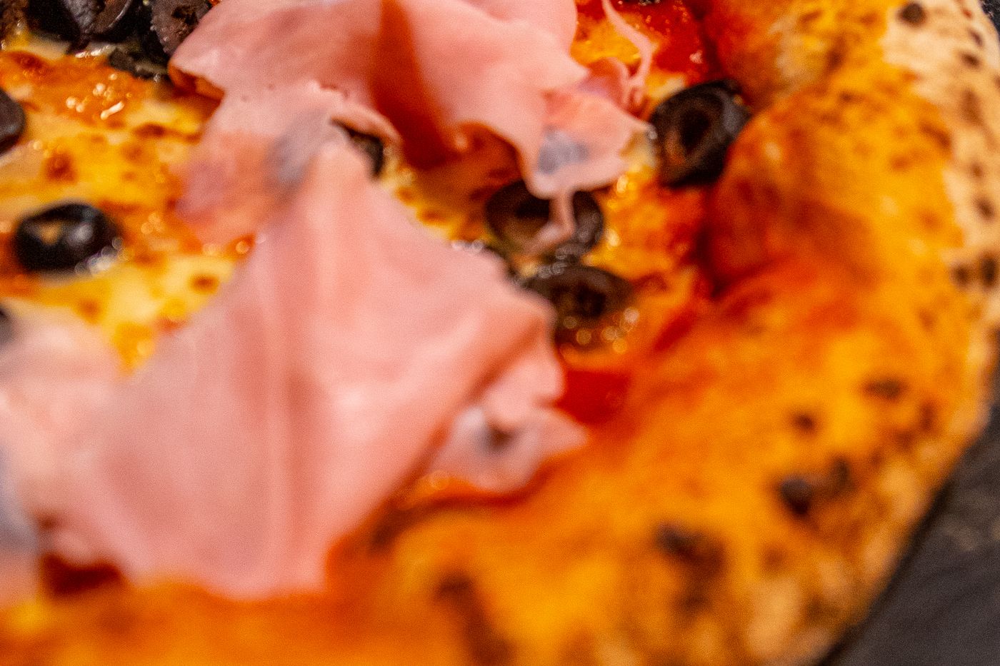 Detalle del jamón y las aceitunas negras sobre la salsa de tomate