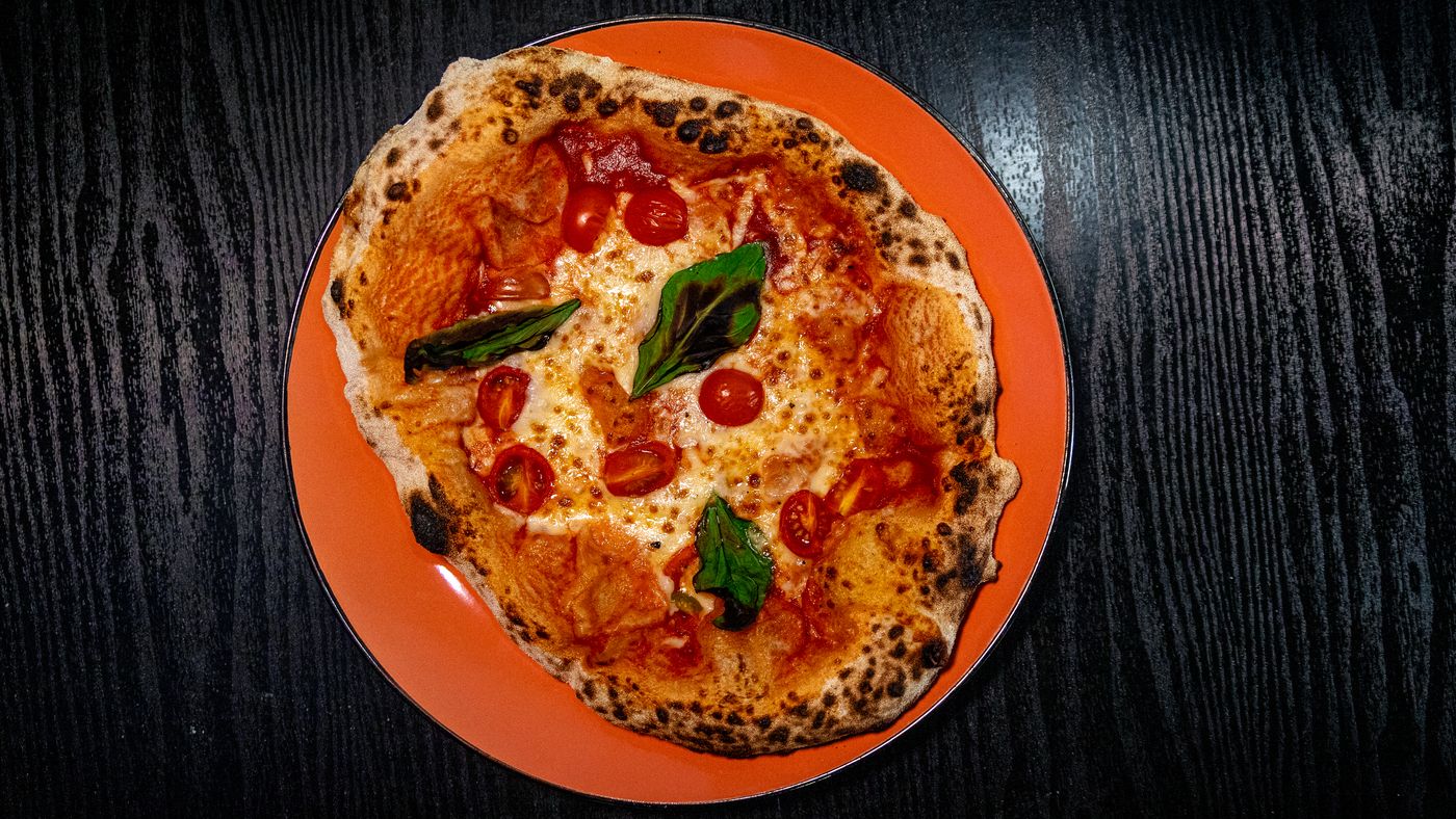 Pizza margherita de masa madre sobre plato de greda naranja, lista para el reparto